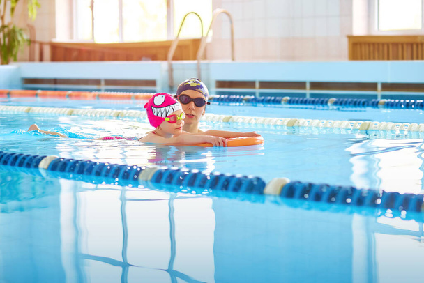 Portret matki lub trenera uczący się pływać z trzepoczącą deską do pływania małą dziewczynką na publicznym basenie. Miejsce na tekst - Zdjęcie, obraz