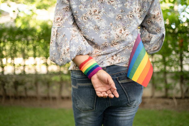 Ασιάτισσα κυρία κρατώντας σημαία ουράνιο τόξο χρώμα, σύμβολο του ΛΟΑΤ μήνα υπερηφάνειας γιορτάζουν ετήσια τον Ιούνιο κοινωνική των γκέι, λεσβία, αμφιφυλόφιλος, τρανσέξουαλ, ανθρώπινα δικαιώματα. - Φωτογραφία, εικόνα