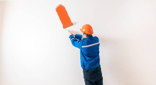 Duvarı silindirle boyayan işçi bir ressam, bir odayı dekore eden bir adam. - Fotoğraf, Görsel