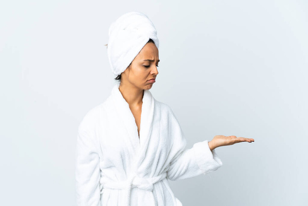 Young woman in bathrobe over isolated white background holding copyspace with doubts - Fotoğraf, Görsel