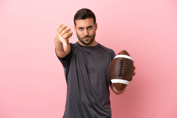 Young caucasian man playing rugby isolated on pink background showing thumb down with negative expression - Foto, Bild