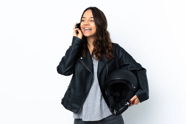 Mladá žena drží motocykl přilbu přes izolované bílé pozadí vedení konverzace s mobilním telefonem - Fotografie, Obrázek