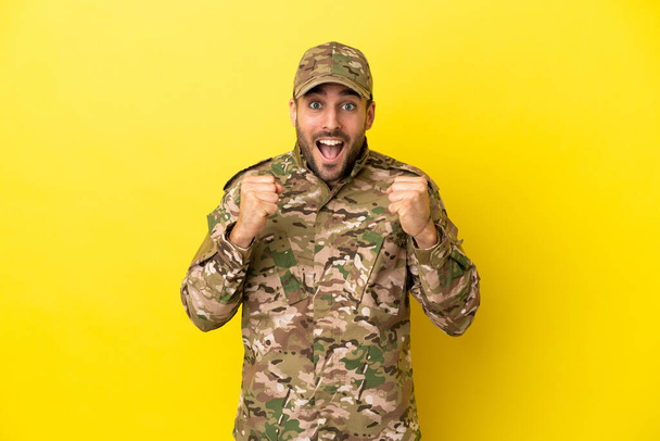 Militar aislado sobre fondo amarillo celebrando una victoria en posición ganadora - Foto, imagen