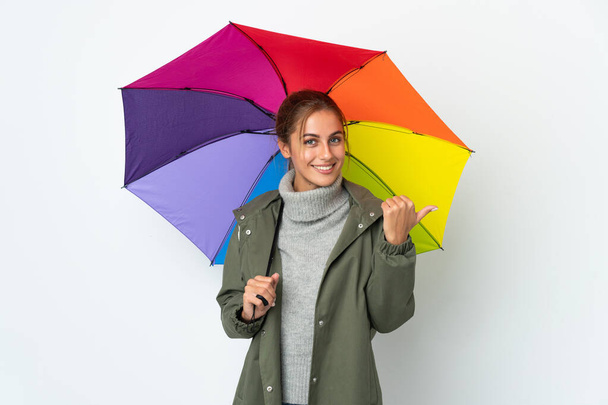 Молода жінка тримає парасольку ізольовано на білому тлі, вказуючи на бік, щоб представити продукт
 - Фото, зображення
