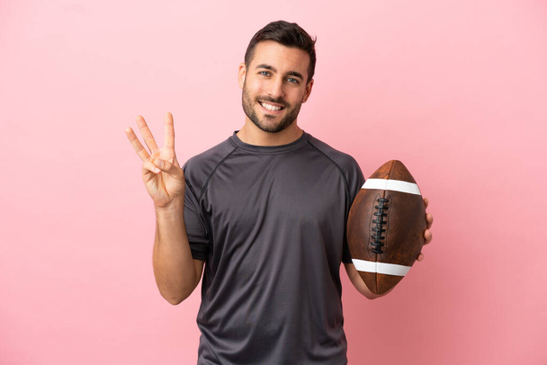 Jeune homme caucasien jouant au rugby isolé sur fond rose heureux et comptant trois avec les doigts - Photo, image