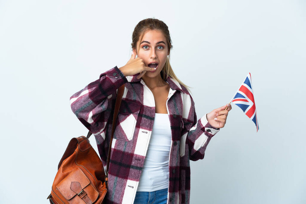 Fiatal nő kezében egy brit zászló elszigetelt fehér háttér így telefon gesztus. Hívj vissza jel. - Fotó, kép