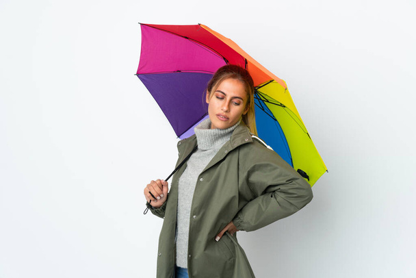 Mujer joven sosteniendo un paraguas aislado sobre fondo blanco que sufre de dolor de espalda por haber hecho un esfuerzo - Foto, imagen