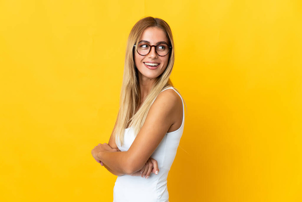 Young blonde woman isolated on yellow background looking to the side and smiling - Foto, Imagem