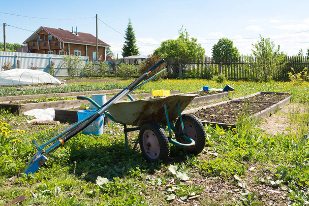 hay una carretilla de jardín con herramientas de jardín junto a los huertos. concepto de agricultura. concepto de vida de granja. - Foto, imagen