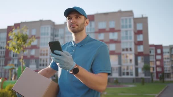 Mężczyzna kurier szuka telefonu komórkowego, aby dostarczyć adres żywności ze sklepu. Dostawca nawiguje przez telefon w mieście, szukając adresów sklepów. Szybkie dostarczenie - Materiał filmowy, wideo