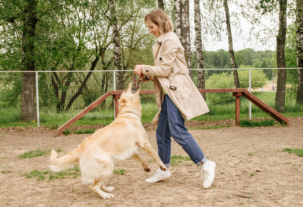 The girl the owner of the dog breed golden retriever plays with her on the playground for walking the dogs - Photo, Image