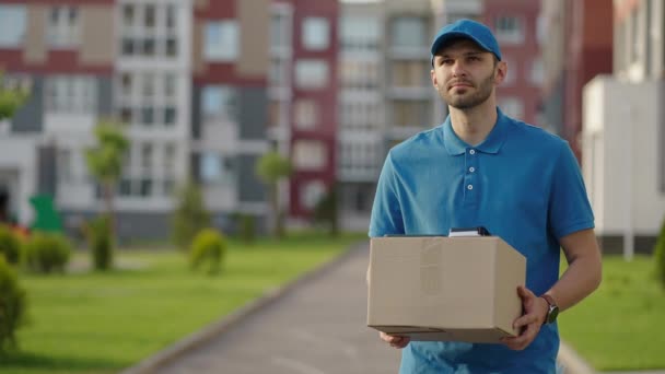 ブルー配達の男は荷物を配達する前に顧客にパッケージを送信します。4kの解像度とスローモーションショット。郵便配達の男が街の通りで小包を手に。郵便の概念。配達サービス. - 映像、動画