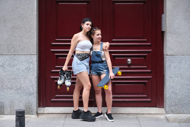 スケートボードを持っている2人の女性と都市のインラインスケート。友達都市生活. - 写真・画像