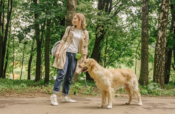 The hostess girl walks in the park with her golden retriever dog - 写真・画像