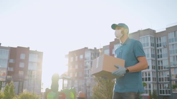 The male deliveryman in masks and protective gloves carries a parcel to the customer with a terminal for contactless payment by mobile phone or NFC card. - Footage, Video