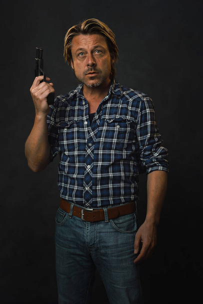 Мужчина с светлыми волосами в рубашке и джинсах лесоруба держит пистолет.. - Фото, изображение
