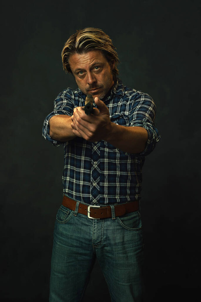 Мужчина с светлыми волосами в рубашке и джинсах-лесорубе целится из пистолета. - Фото, изображение