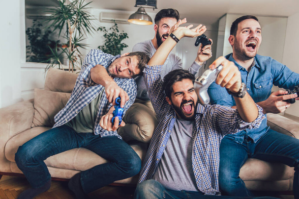 Hymyilevät miespuoliset ystävät pelaavat videopelejä kotona - Valokuva, kuva