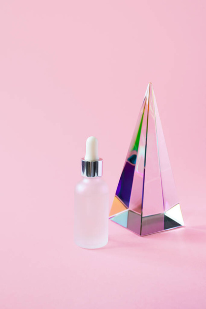 Serum pot met pipet mockup en glazen piramide prisma op roze achtergrond met kopieerruimte, verticaal. Schoonheidsverzorging cosmetisch product trendy minimalisme - Foto, afbeelding