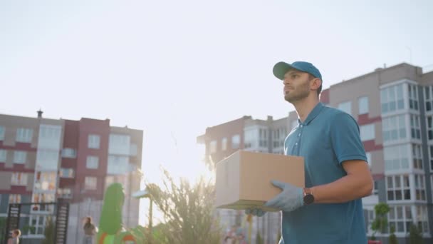 Blue delivery man send a package to customer on before deliver cargo. 4k resolution and slow motion shot. Male postman with parcel in hands at city street. Postal concept. Delivery service. - Footage, Video
