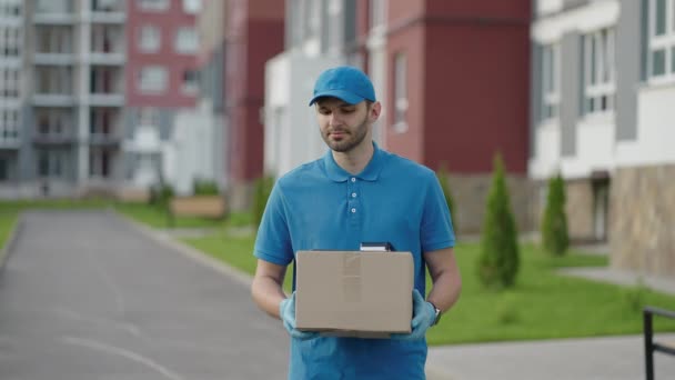 ブルー配達の男は荷物を配達する前に顧客にパッケージを送信します。4kの解像度とスローモーションショット。郵便配達の男が街の通りで小包を手に。郵便の概念。配達サービス. - 映像、動画