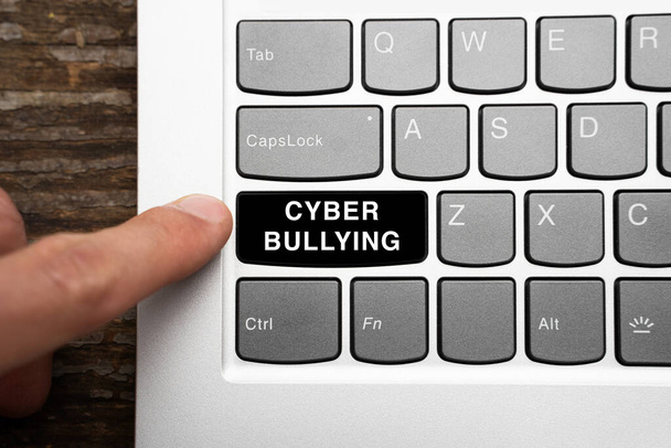 Finger reichen, um eine schwarze Taste mit dem Wort Cybermobbing auf einer Computertastatur zu drücken. Cybermobbing unter Nutzern beliebter sozialer Netzwerke - Foto, Bild