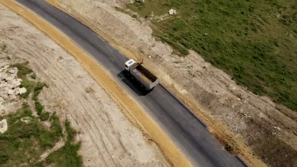 Feche a mineração pesada caminhão de descarga branco de quatro eixos dirigindo por nova estrada pavimentada para a mina com areia - Filmagem, Vídeo