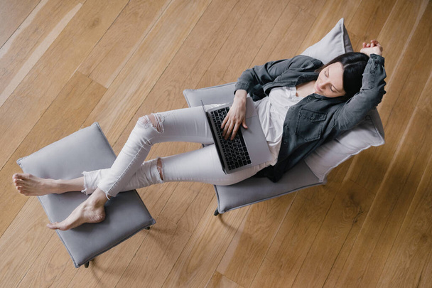 top view, europejska kobieta biznesu w szarej koszuli i białych dżinsach siedząca na krześle, pracująca z laptopem i rozmawiająca przez telefon, SMS-ująca, surfująca po Internecie lub robiąca zakupy online - Zdjęcie, obraz