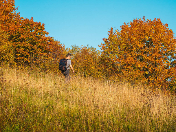 Мужчина средних лет с рюкзаком спускается с осеннего холма. - Фото, изображение