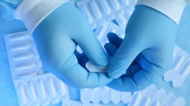 Profesjonalny proktolog w niebieskich rękawiczkach medycznych otwiera czopki na hemoroidy na niebieskim tle wielu innych leków. Doktor pokazuje świece do leczenia hemoroidów. Zbliżenie. Widok z góry - Materiał filmowy, wideo