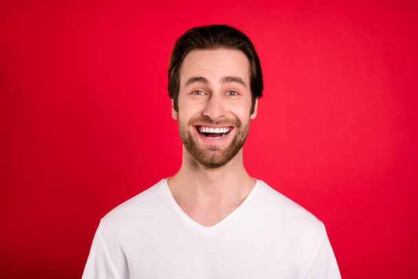 Photo of funny young brown hairdo man laugh wear white t-shirt isolated on vivid red color background - Foto, Imagem