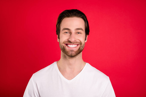 Фото очаровательной молодой веселый счастливый мужчина улыбается хорошее настроение носить белую рубашку изолированы на красном фоне - Фото, изображение