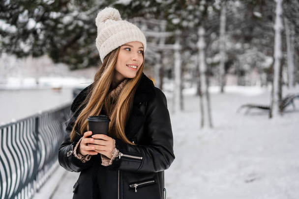 Happy beautiful girl drinking coffee takeaway while walking in winter park - Foto, Imagem