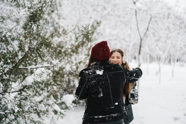 Happy beautiful girls playing snowballs while walking in winter forest - Fotografie, Obrázek