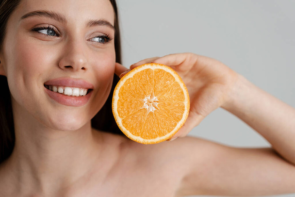 Happy shirtless girl smiling while posing with orange isolated over white background - 写真・画像