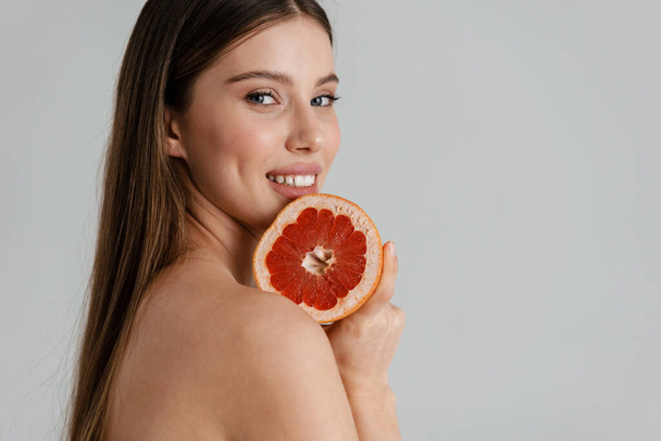 Feliz chica sin camisa sonriendo mientras posando con pomelo aislado sobre fondo blanco - Foto, Imagen