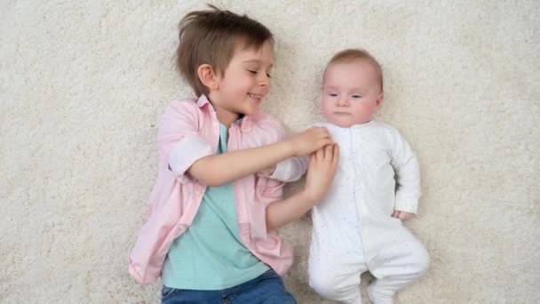 Gelukkig lachende jongen liggend met zijn broertje op tapijt en plezier hebben. Kinderen geluk en familierelaties. - Video