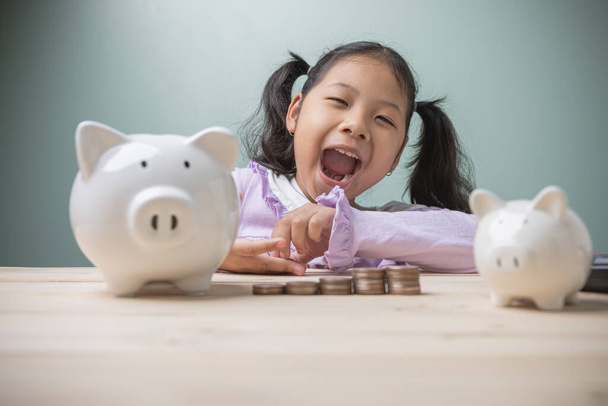 Roztomilé asijské dítě úsměv štěstí je počítání peněz na pokles prasečí banky s černou kalkulačku umístěnou na starém dřevěném stole. Koncepce ušetřit peníze na vzdělávání budoucnosti. - Fotografie, Obrázek