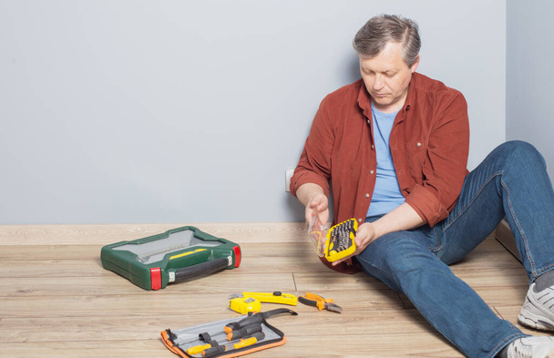 middle-aged man with  set of repair tools on wooden floor - Фото, изображение