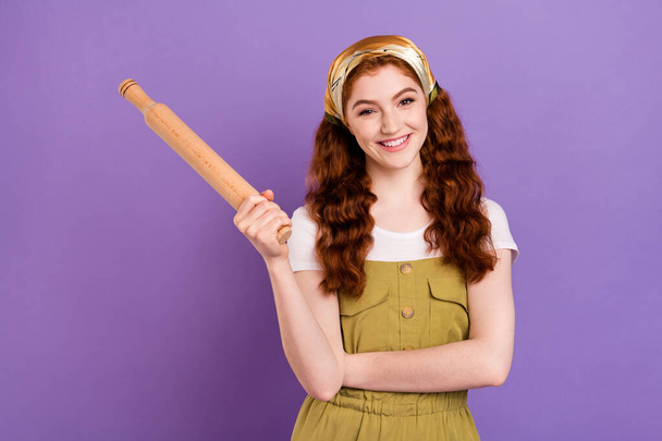 Photo of cheerful young nice pretty lady hold hand rolling pin smile cook kitchen isolated on purple color background - Fotó, kép