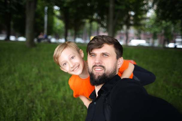 der Vater und das Kind werfen ein Selfie in die Kamera und lachen fröhlich, hinter dem das Kind steht - Foto, Bild