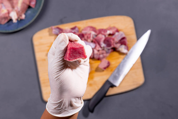 Meat cutting , a man cutting beef meat  wearing glouse on wooden board with grey textured background,topview. - Foto, Bild