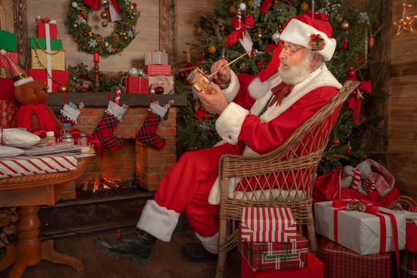 Άγιος Βασίλης κάνοντας παιχνίδια στο εργαστήριο σε εορταστικό εσωτερικό εσωτερικό ξύλινο σπίτι, χαρούμενη διάθεση Πρωτοχρονιάς Πνεύμα των Χριστουγέννων. Ανώτερος άνθρωπος με πραγματική λευκή γενειάδα cosplay Άγιος Βασίλης. - Φωτογραφία, εικόνα