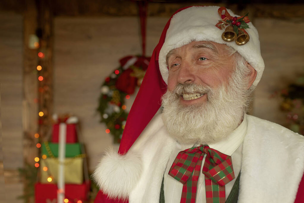 Santa Claus ve slavnostním interiéru v dřevěném domě, novoroční veselá nálada Spirit of Christmas. Starší muž se skutečným bílým plnovousem kostým Otec Vánoce. - Fotografie, Obrázek