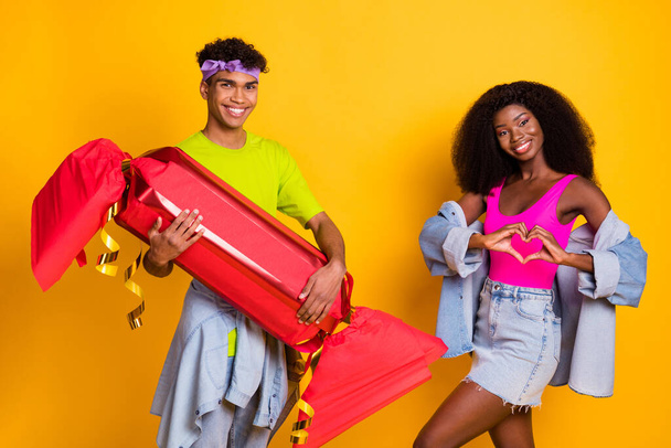 Photo of shiny flirty young couple dressed denim outfit holding huge candy showing fingers heart isolated yellow color background - Zdjęcie, obraz