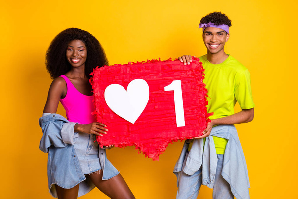 Photo of pretty beautiful young couple dressed denim outfit dancing holding huge like sign isolated yellow color background - Foto, Imagem
