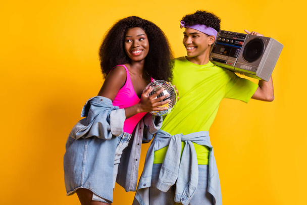 Portrait of attractive cheerful funky couple embracing having fun carrying retro player isolated over bright yellow color background - Fotoğraf, Görsel