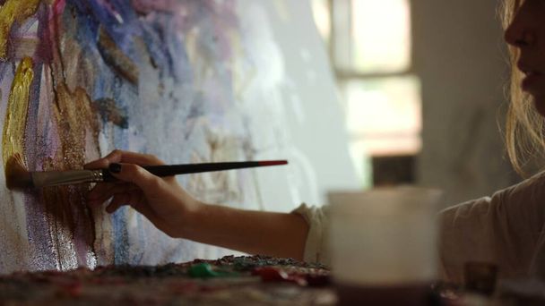 Жінка-художник тримає пензлик в студії. Жінка створює картинку в приміщенні
. - Фото, зображення