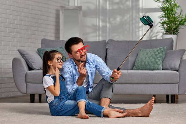 father and child holding paper glasses on stick and take a selfie - Фото, изображение