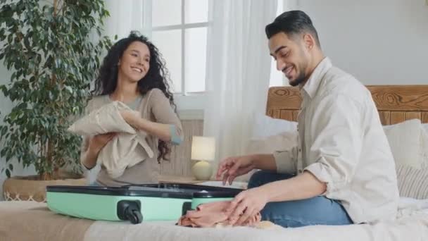 Hispánský latinský pár novomanželé manželé kudrnatý žena a šťastný muž sedí na posteli doma ložnice dávat věci ve velkých kufříků zavazadla připravit na cestu do zahraničí dovolená chlap ukazující palce nahoru - Záběry, video
